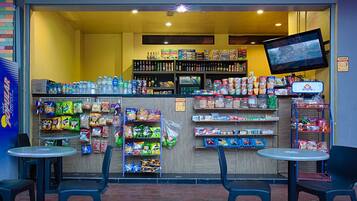 Una tienda de conveniencia con estantes llenos de aperitivos, bebidas y otros productos. Hay dos mesas y sillas afuera.