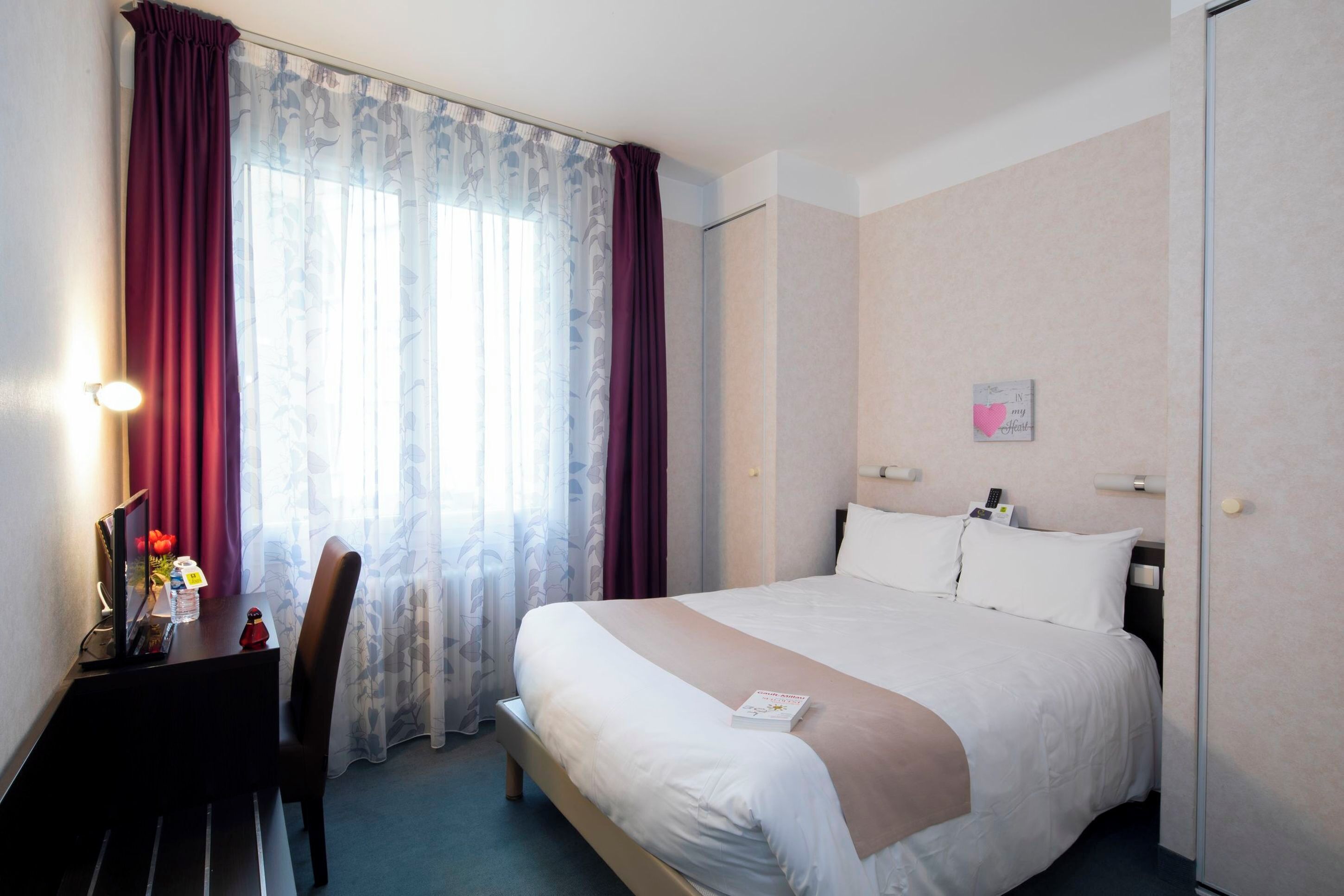 Una habitación de hotel con cama, escritorio, computadora y silla.