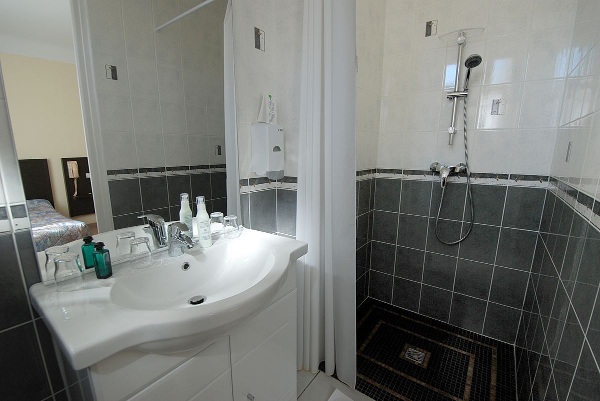 A bathroom with a white sink, a mirror, a shower with a handheld showerhead, and a tiled floor.