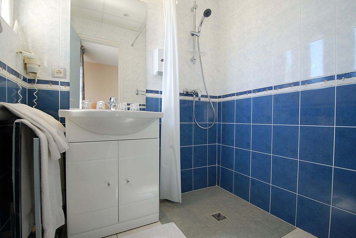 Une salle de bain avec un lavabo blanc, des murs recouverts de carreaux bleus, une douche et un miroir.