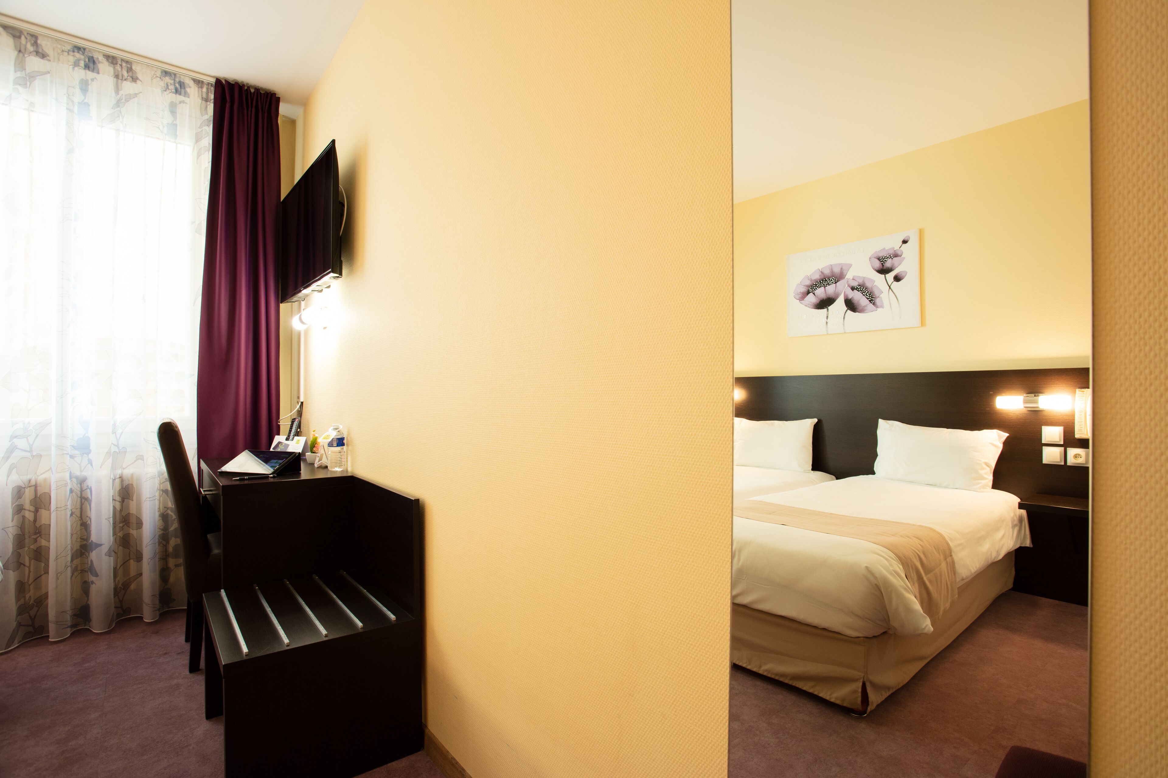 A hotel room with a bed, a desk, a chair, a TV, and a painting on the wall.