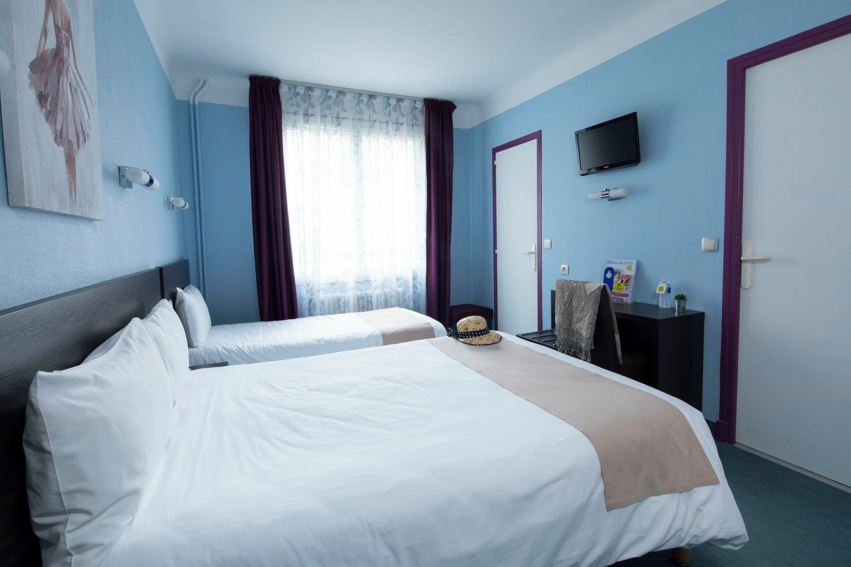 Ett hotellrum med två sängar, en tv, ett skrivbord och ett fönster med gardiner.
