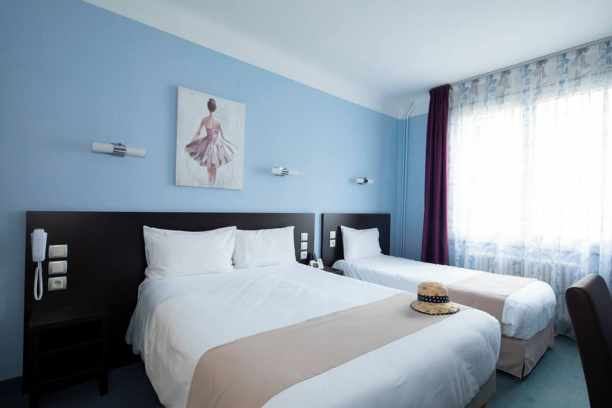 Quarto de hotel com duas camas, um quadro na parede, um telefone e uma janela com cortinas.