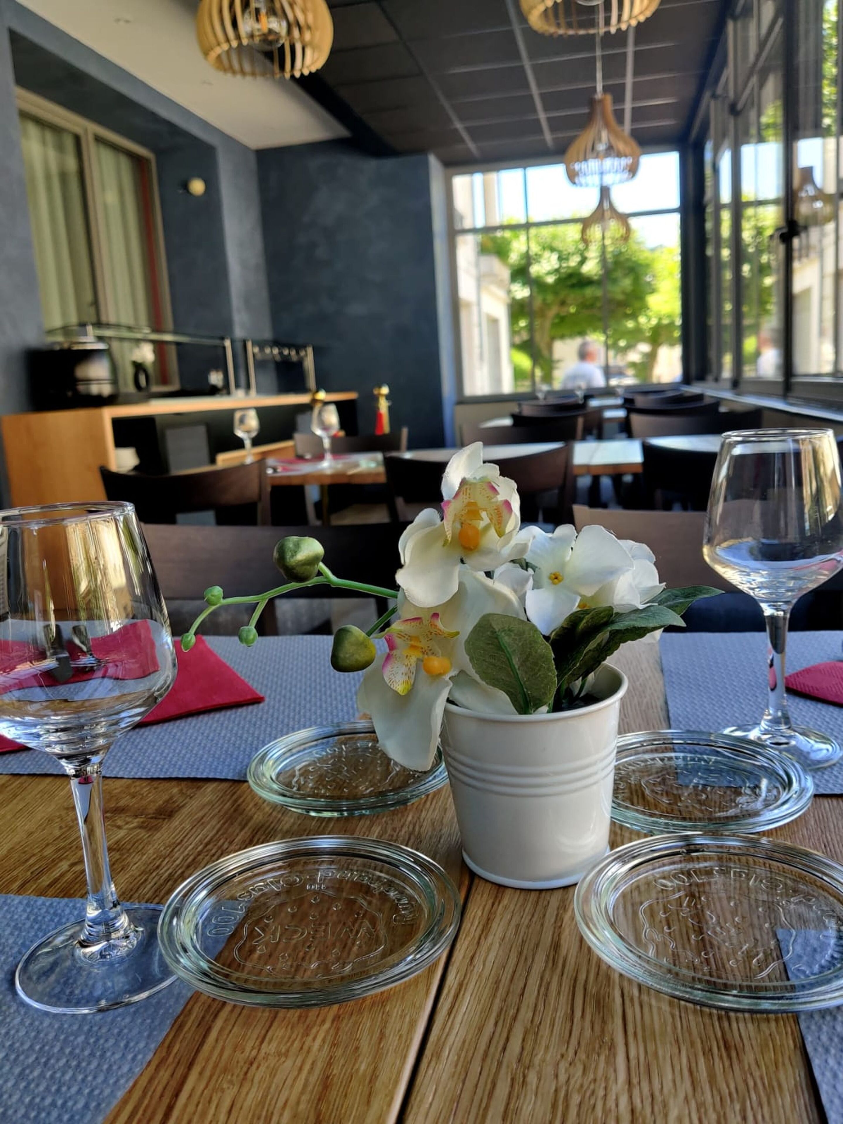 A table with a potted orchid, wine glasses, and a glass plate with a logo.