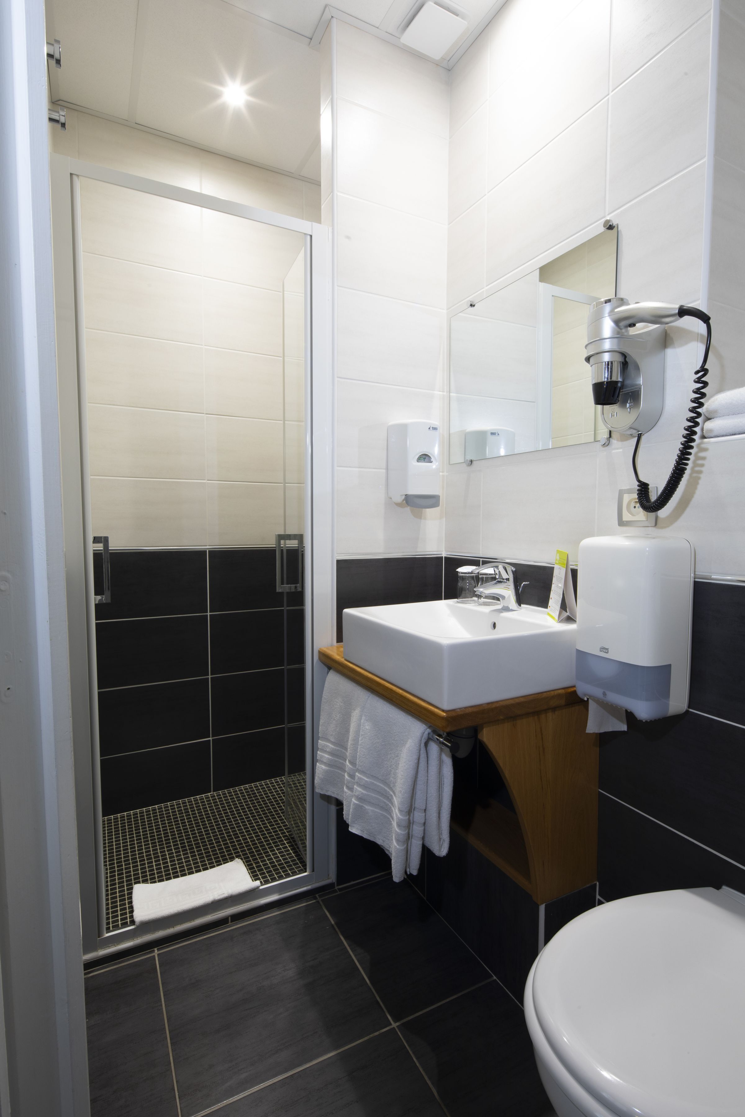 A modern bathroom with a glass shower enclosure, a sink with a mirror, and a hairdryer mounted on the wall.