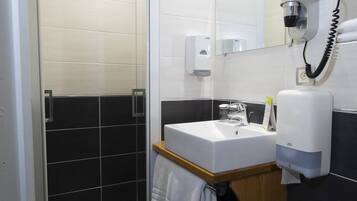 A modern bathroom with a glass shower enclosure, a sink with a mirror, and a hairdryer mounted on the wall.