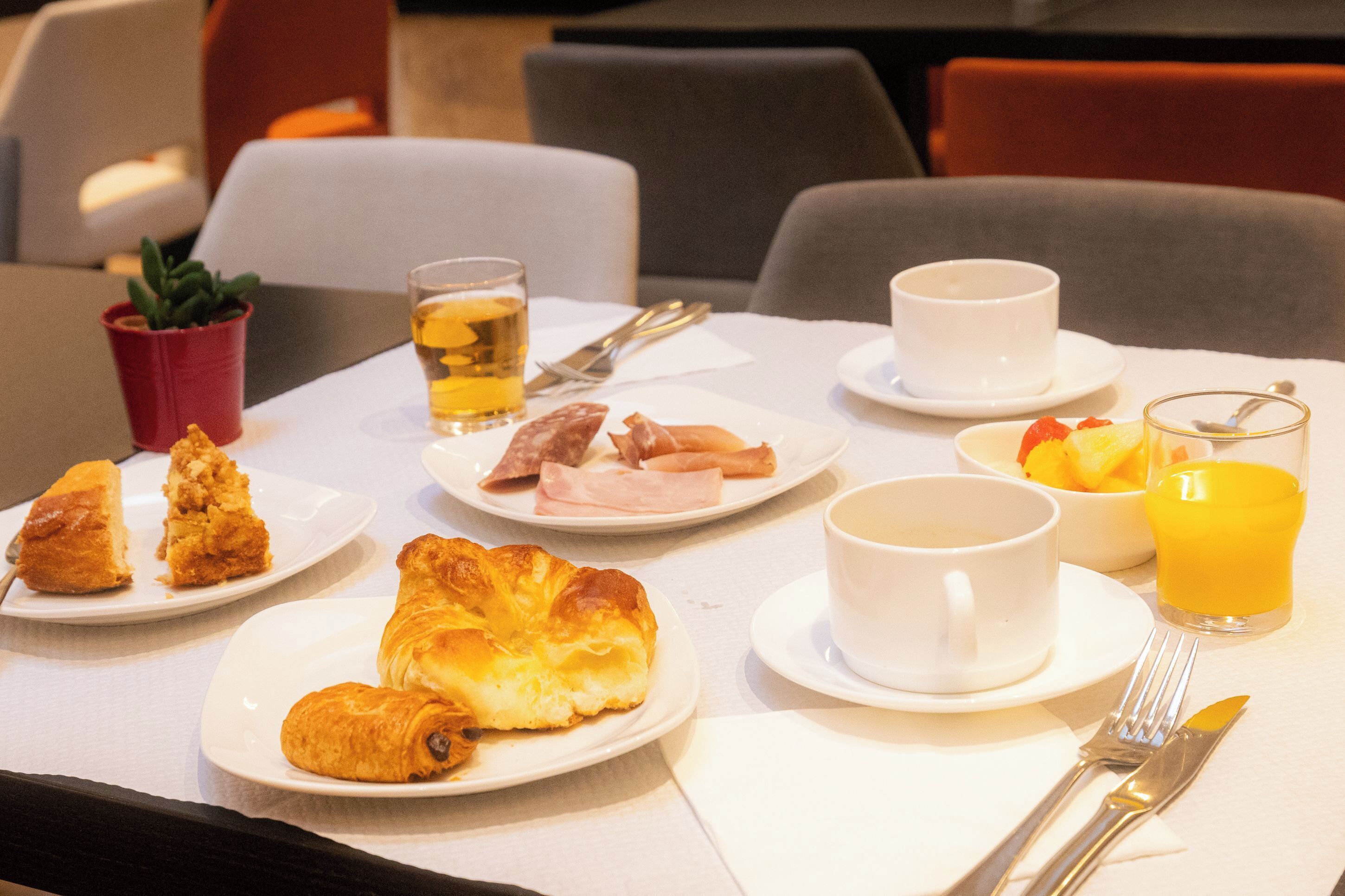 Une table dressée pour le petit-déjeuner, avec des assiettes de viennoiseries, des fruits et des boissons.