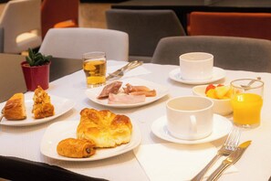 Ein Frühstückstisch mit Tellern voller Gebäck, Früchten und Getränken.