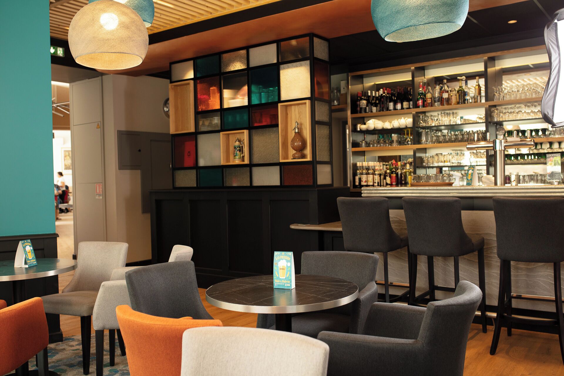 Un espace bar avec des tables et des chaises rondes, une étagère remplie de bouteilles et un mur orné de tableaux.
