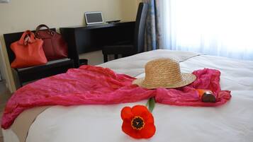 Habitación de hotel con cama, una laptop en un escritorio, un bolso rojo, un sombrero de paja, una flor roja y una vela.