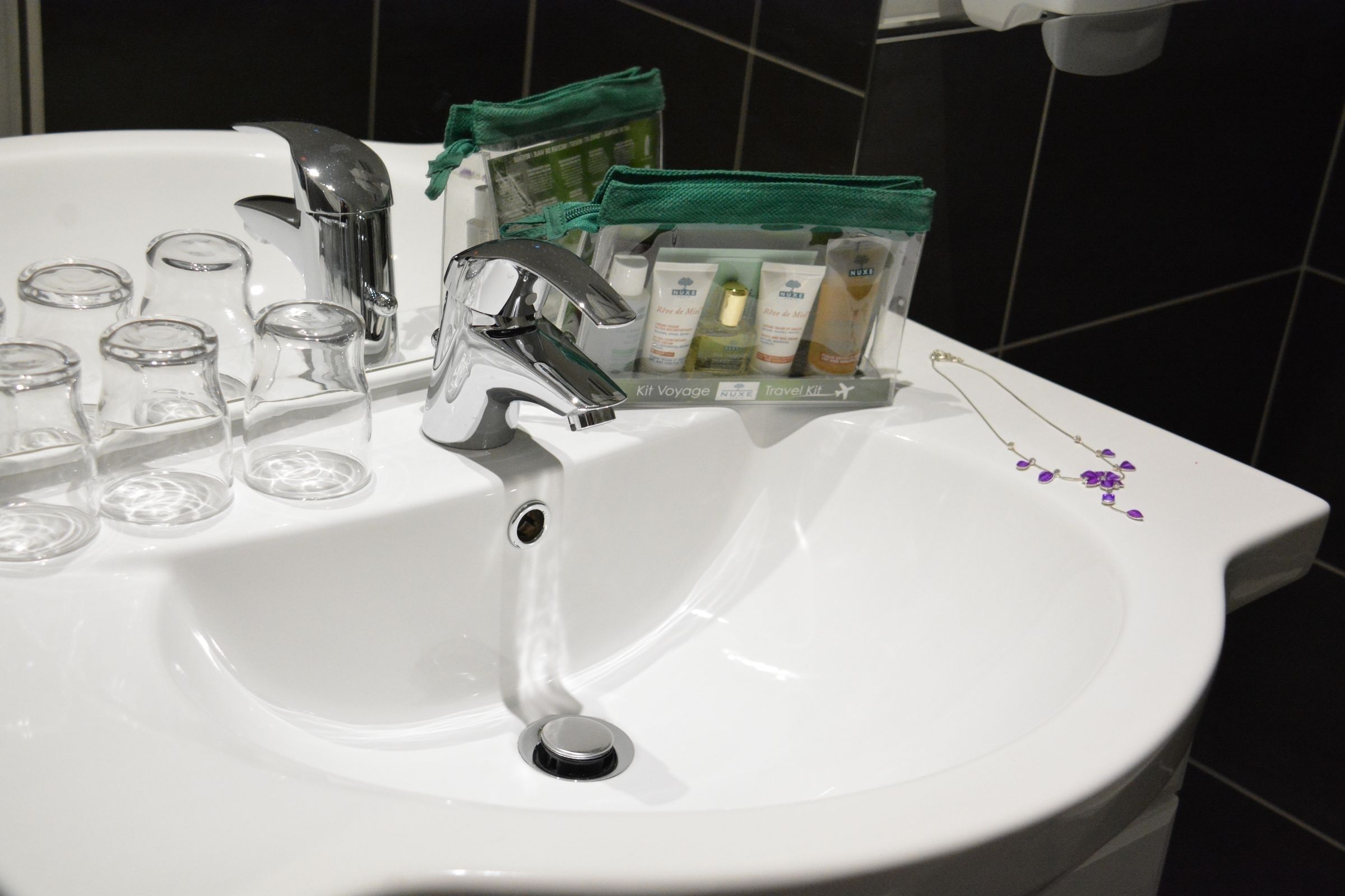 A white bathroom sink with a chrome faucet, a mirror, and a green toiletry bag on the counter.