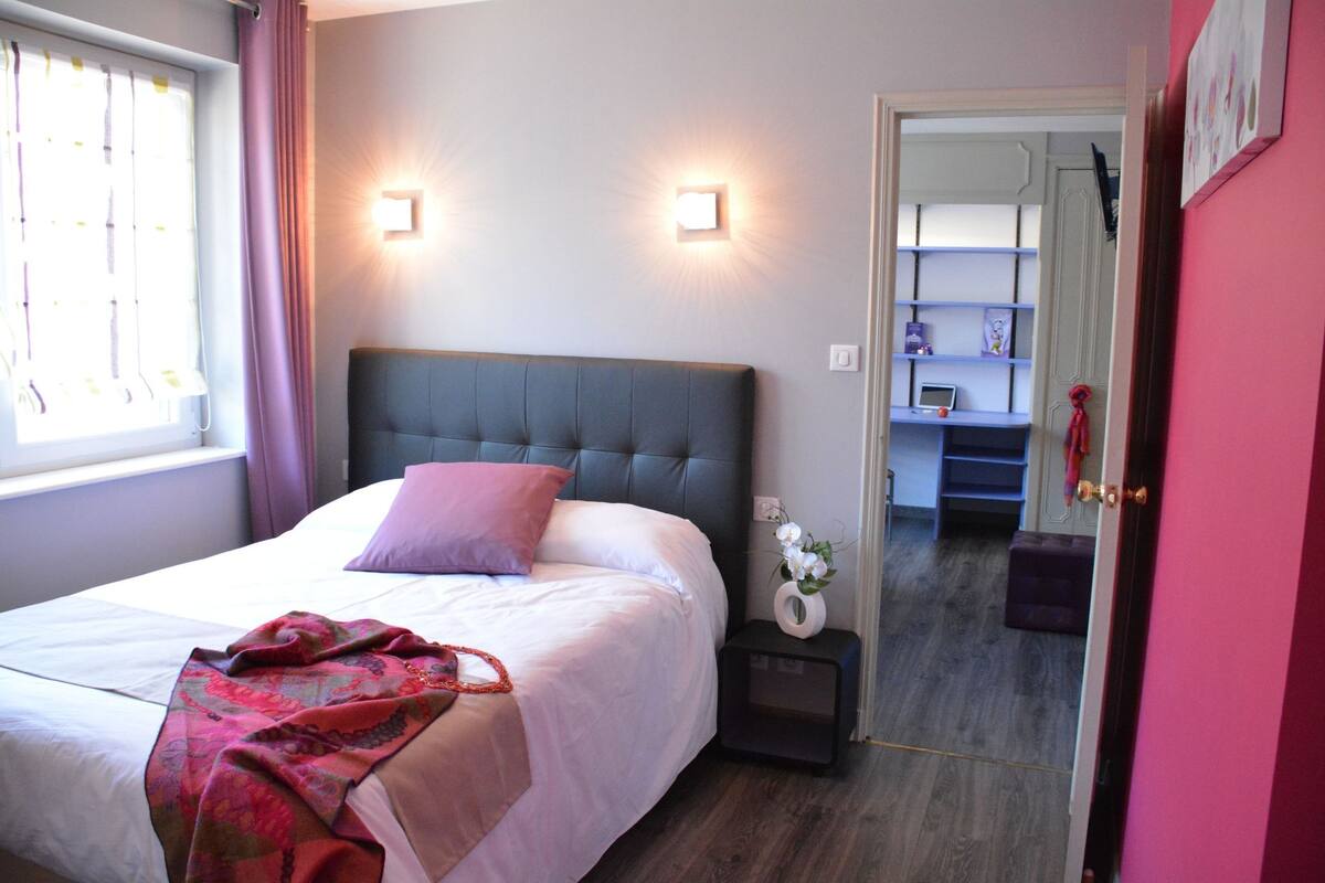 Quarto com cama, mesa de cabeceira e criado-mudo com um vaso de flores.
