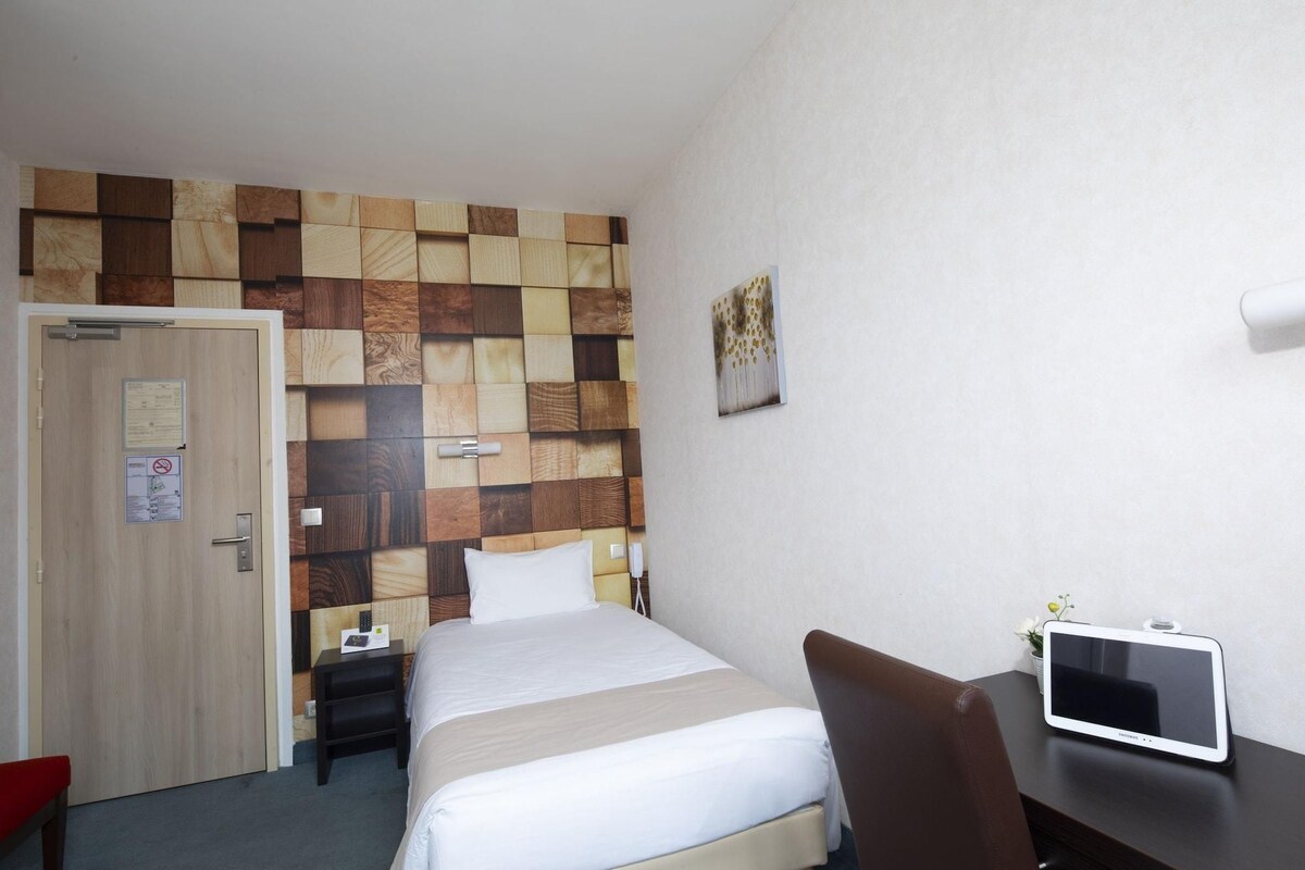 Habitación de hotel con cama, mesita de noche, silla, televisor y un panel de madera en la pared.