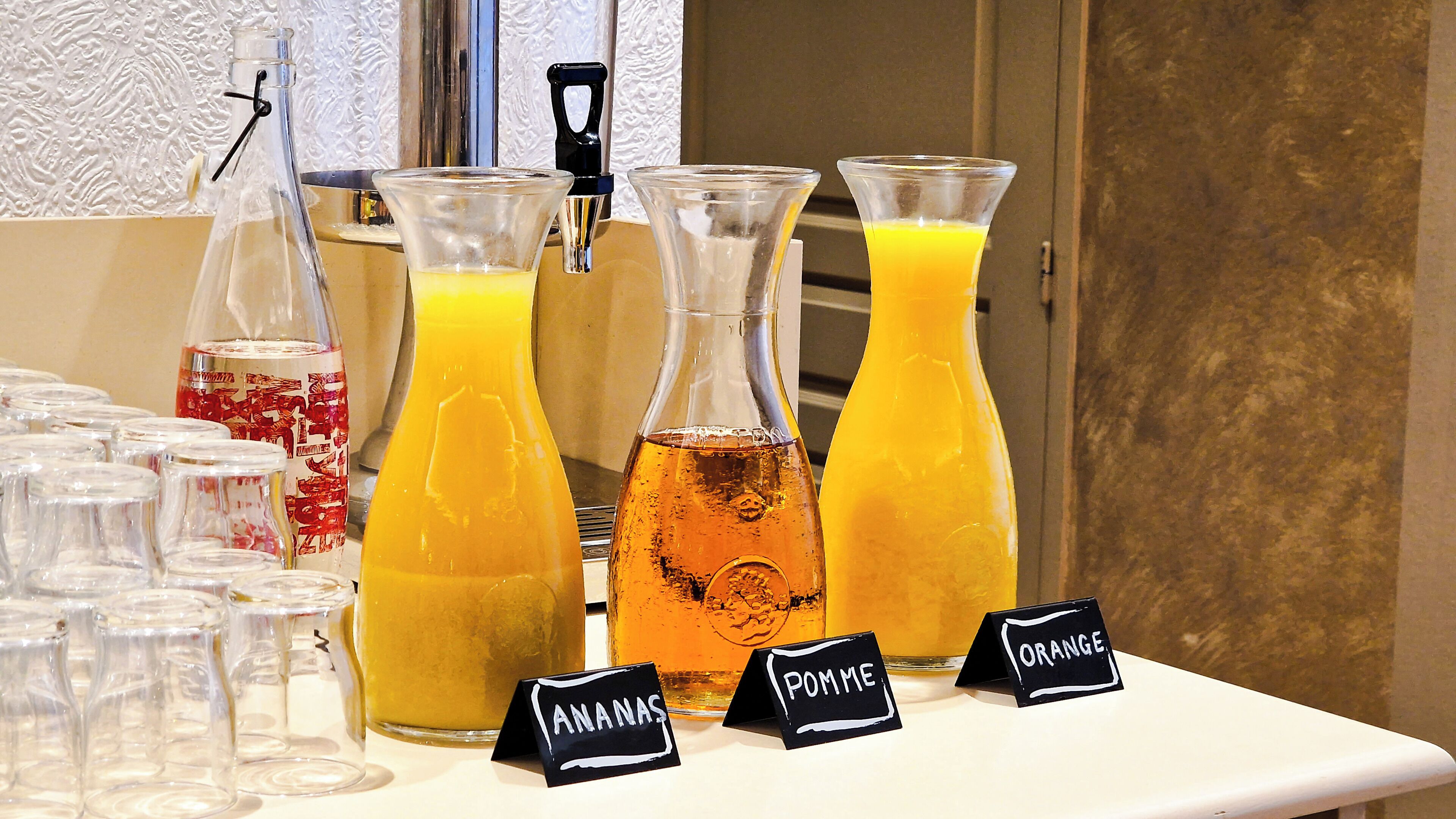 Ein Getränkeangebot mit beschrifteten Karaffen mit Orangensaft und Granatapfelsaft sowie einer Auswahl an Gl äsern.