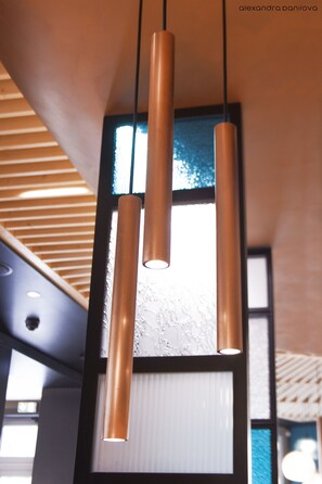 Ein modernes Interieur mit einer Holzbalkendecke, einem großen Fenster mit Aussicht und drei zylindrischen Pendelleuchten.