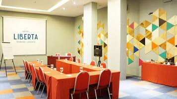 Un salón de conferencias con una larga mesa, sillas, una pantalla de proyector y un diseño geométrico colorido en la pared.
