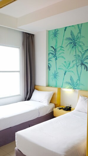A hotel room with two beds, a window with curtains, a wall with a palm tree mural, and a nightstand with a remote control.