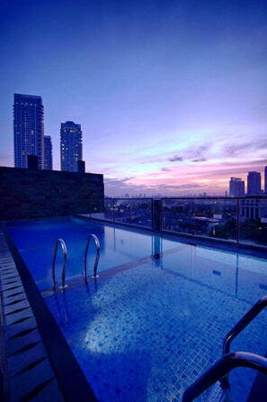 A rooftop infinity pool with clear glass railings, offering a city skyline view at dusk. - Liberta Hotel Kemang (Jakarta)