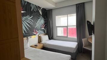 A hotel room with two beds, a desk, a chair, a TV, and a window with curtains.