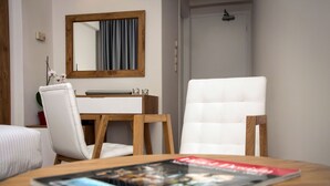 Habitación de hotel con cama, un escritorio con espejo, una silla blanca y una revista sobre la mesa.