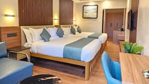 A hotel room with a large bed, a desk, a chair, a TV, and a ceiling fan. - Camelot Resort (Devikolam)