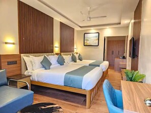 A hotel room with a large bed, a desk, a chair, a TV, and a ceiling fan. - Camelot Resort (Devikolam)