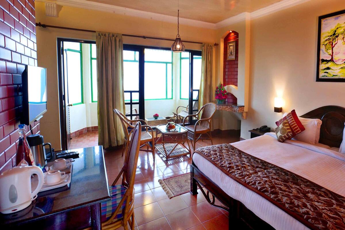 Une chambre d’hôtel comprenant un lit, une table à manger avec des chaises, un coin café et une grande fenêtre avec des rideaux.