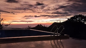 A swimming pool with a view of a sunset over a mountainous landscape. - Camelot Resort (Devikolam)