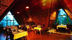 A dining area with tables and chairs, large windows, and a high, sloped ceiling. - Camelot Resort (Devikolam)