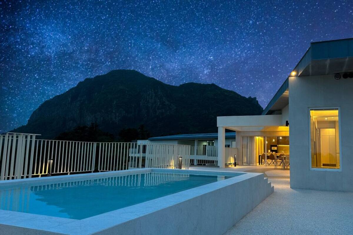 A modern building with a pool and a mountain backdrop under a starry sky.