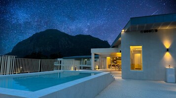 Un edificio moderno con piscina y montañas al fondo, bajo un cielo estrellado.
