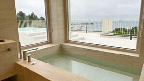 A bathroom with a large window, a bathtub, and a view of a pool and outdoor area. - Y Resort Jeju (Seogwipo)