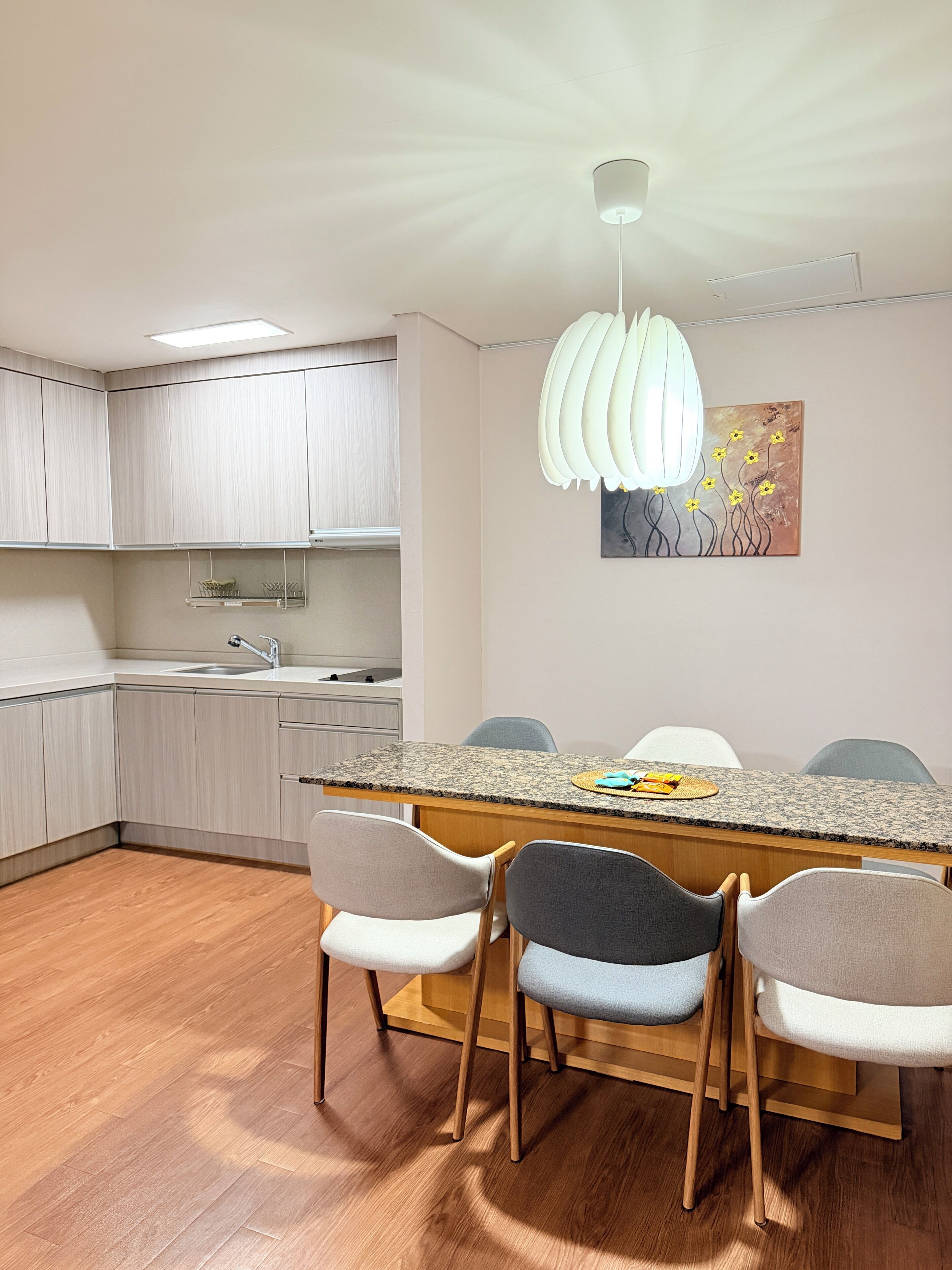 Une cuisine moderne dotée d’un plan de travail en granit, de meubles en bois, d’un évier encastré et d’un coin repas avec quatre chaises.