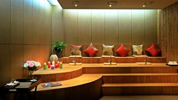 Zona de recepción con un mostrador curvo de madera, varios lavamanos y un banco con cojines decorativos.