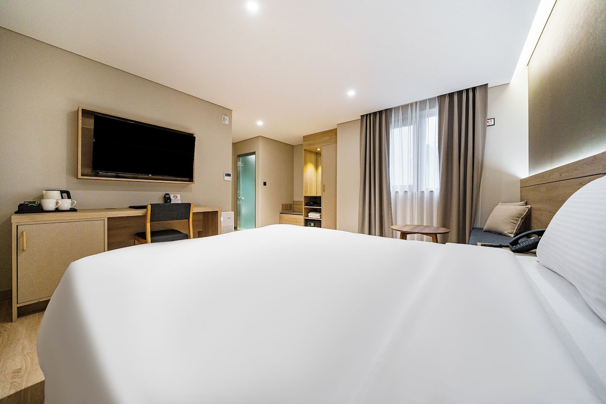 Ein Hotelzimmer mit einem großen Bett, einem Schreibtisch mit Stuhl, einem Fernseher und einem kleinen Tisch mit Telefon.