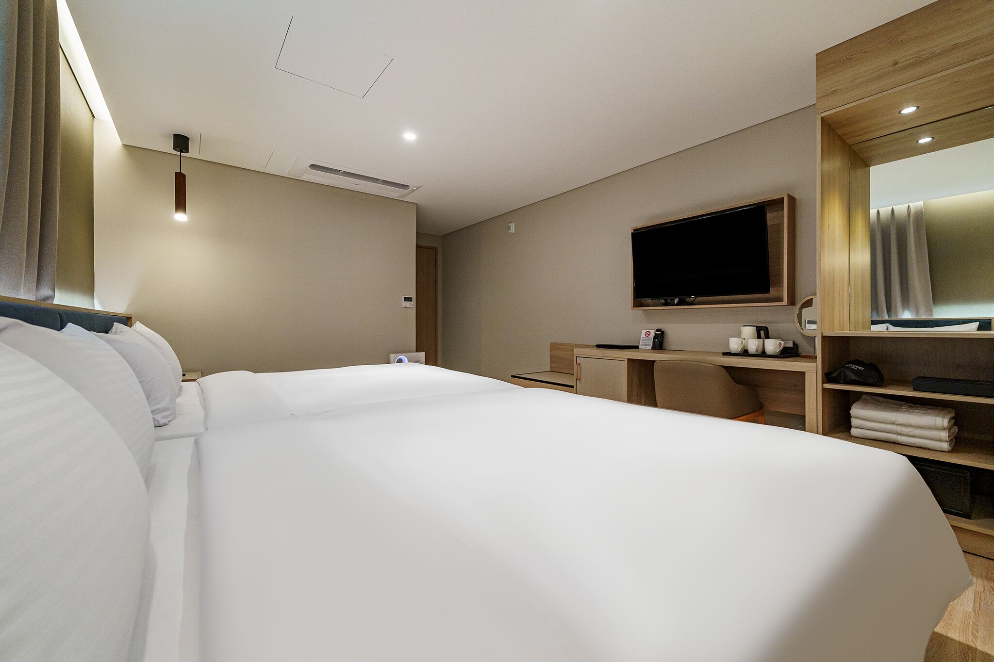 Et moderne hotelværelse med en stor seng, et skrivebord, et fladskærms-tv og et spejl.