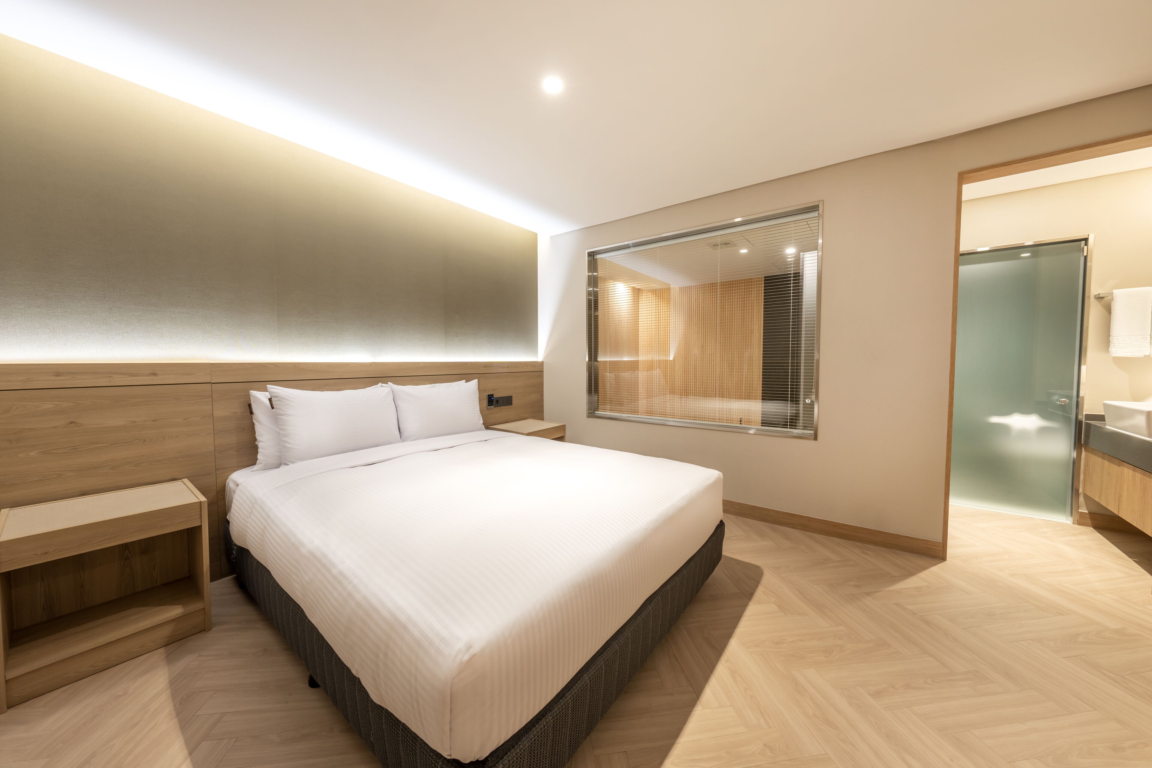 Ein modernes Schlafzimmer mit einem großen Bett, einem Holzkopfende, Nachttischen und einer Duschkabine aus Glas.