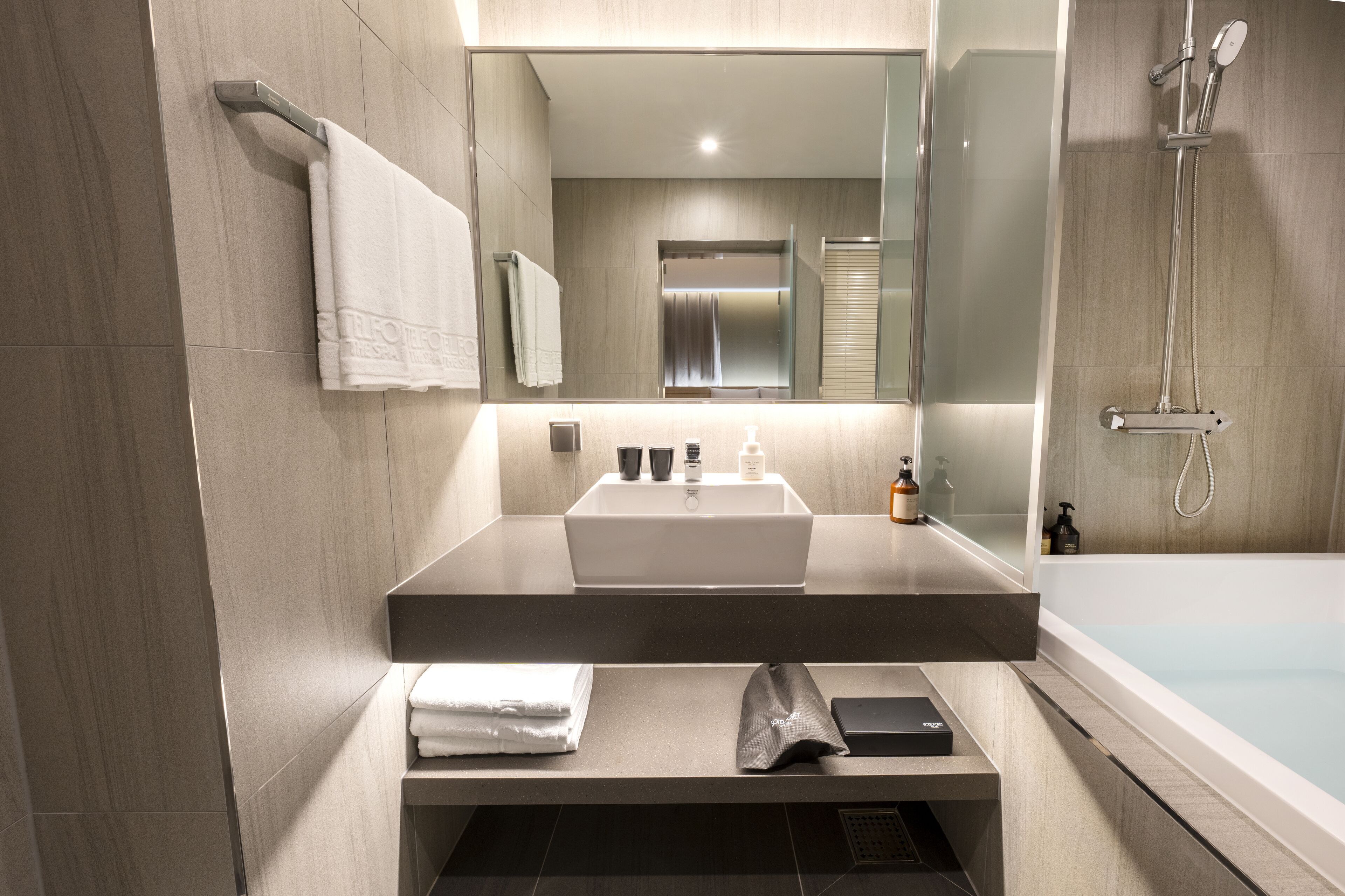 A modern bathroom with a large mirror, a sink, a shower, and a towel rack.