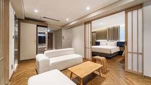 A modern hotel room with a wooden floor, a sofa, a small table, and a bed with a nightstand. - HOTEL FORÊT THE SPA (Busan)