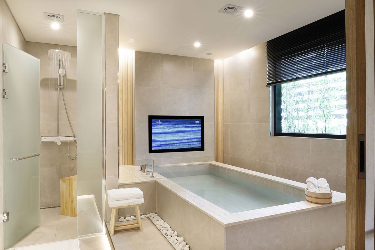 Ein modernes Badezimmer mit einer großen Badewanne, einer Dusche und einem an der Wand befestigten Fernseher.