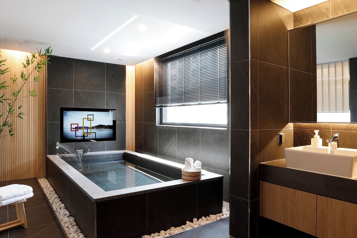Ein modernes Badezimmer mit einer großen Badewanne, einem Waschbecken und einem an der Wand befestigten Fernseher.