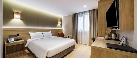 A modern hotel room with a large bed, bedside table with a phone, a desk with a TV, and a window with curtains.