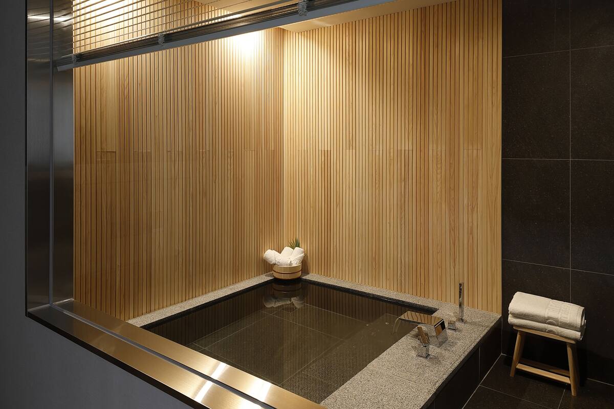 Ein modernes Badezimmer mit einer Wand aus Holzpaneelen, einer Glaskabine mit Badewanne, einer Arbeitsplatte aus Granit und einem hölzernen Hocker.