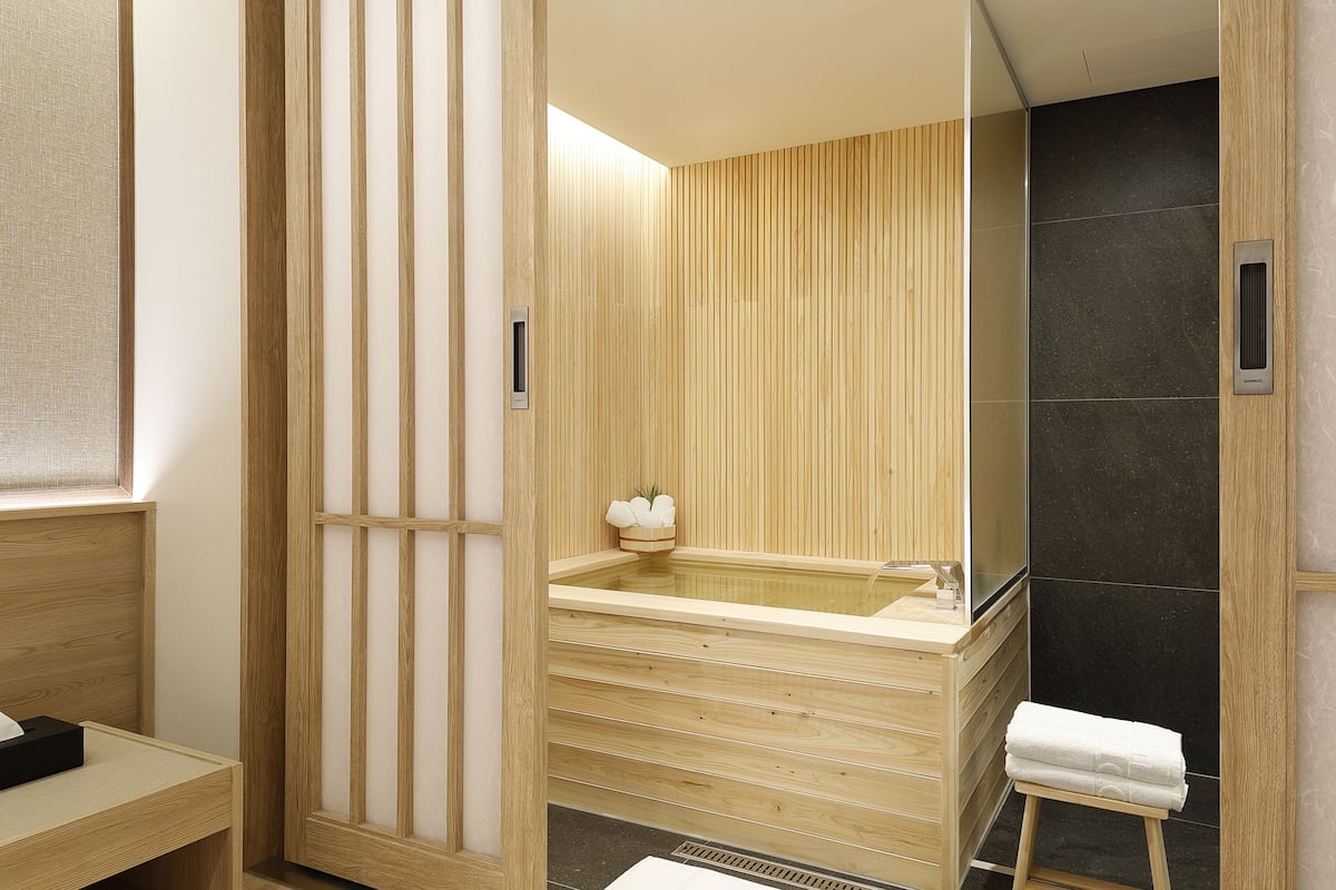 Ein modernes Badezimmer mit einem Holzmöbelstück, einer freistehenden Badewanne und einer ebenerdigen Dusche mit dunklen Fliesen.