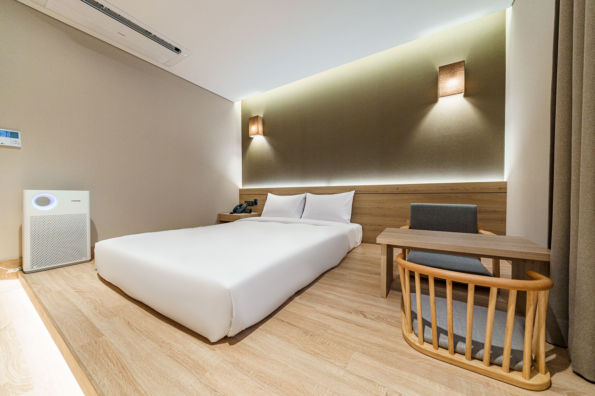 Quarto de hotel com uma cama grande, mesa de cabeceira e uma pequena escrivaninha com cadeira.