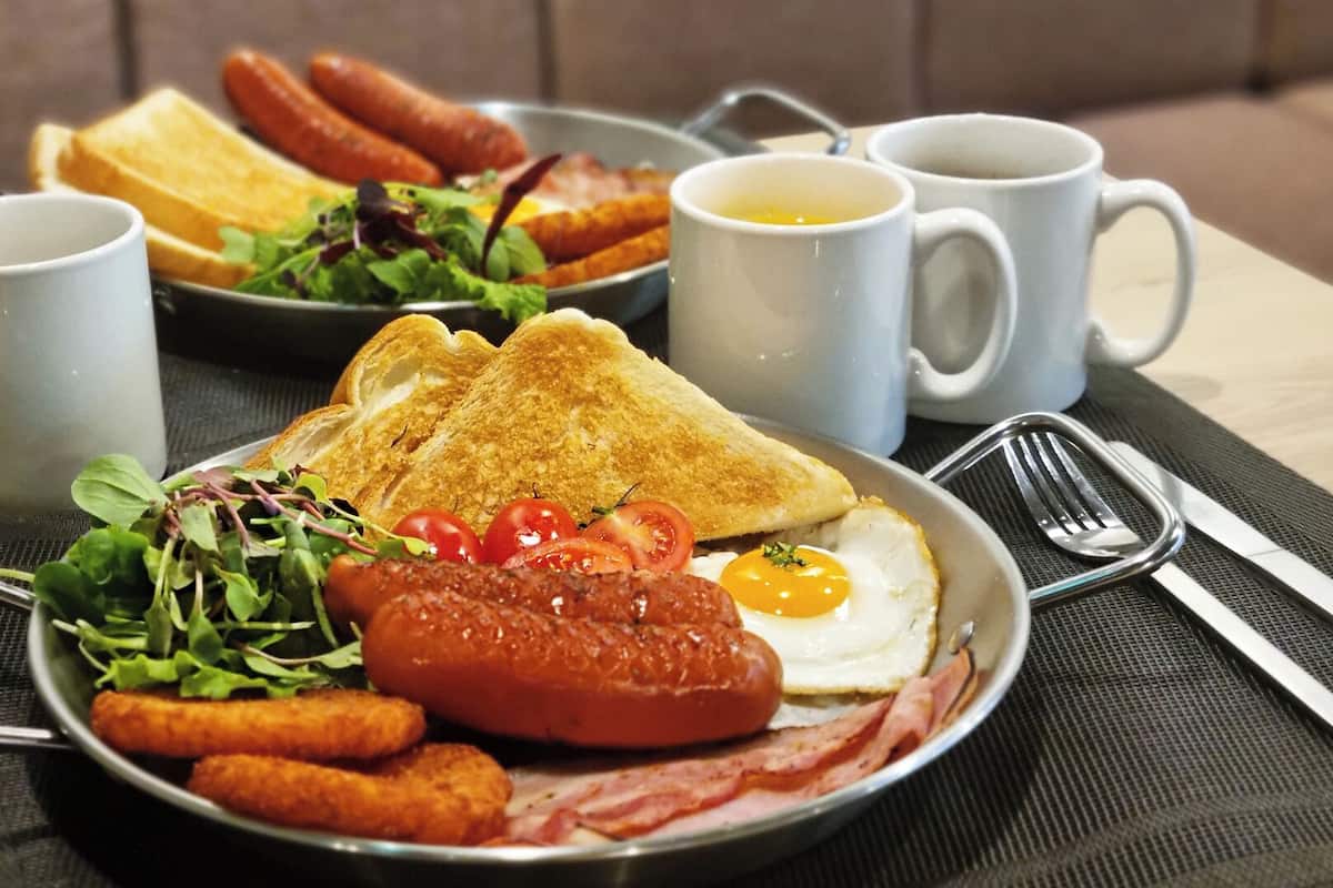 Ein Frühstücksteller mit Toast, Eiern, Tomaten, Salat und Würstchen.