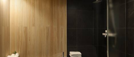 A modern bathroom with a wooden panel wall, a black tiled shower area, and a small stool with a towel.