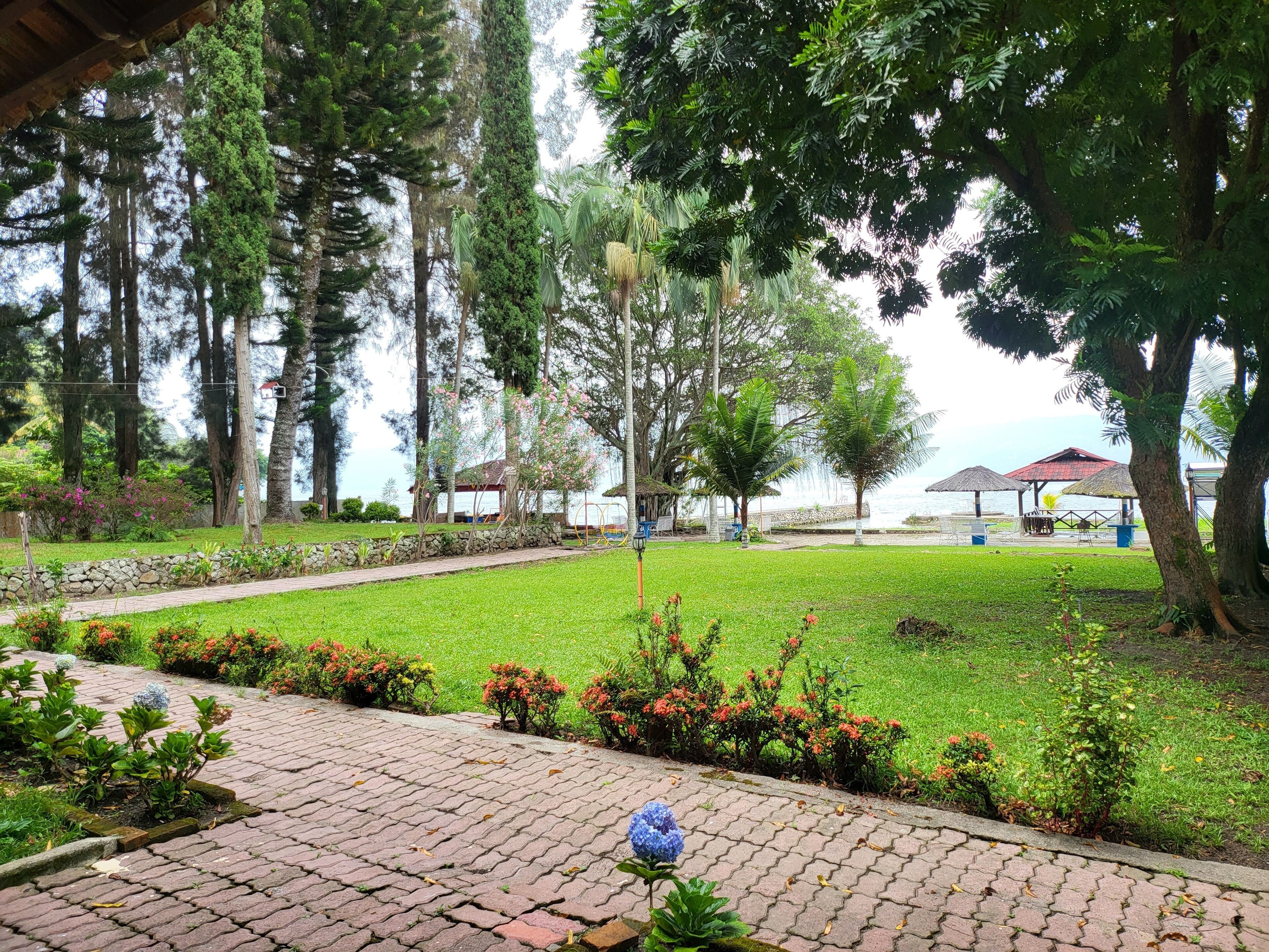 A well-maintained garden with a paved walkway, a gazebo, and a view of the sea.