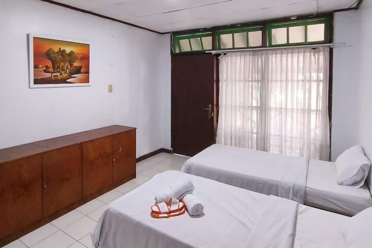 A hotel room with two beds, a wooden cabinet, a painting on the wall, and a window with curtains.
