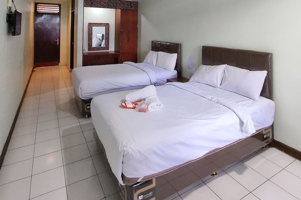 A hotel room with two beds, a wooden headboard, a tiled floor, and a door leading to a hallway.